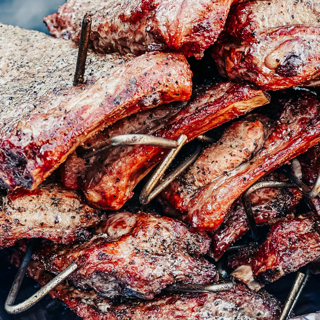 Many racks of pork ribs piled with hooks from the Rib Hanger Kit in them